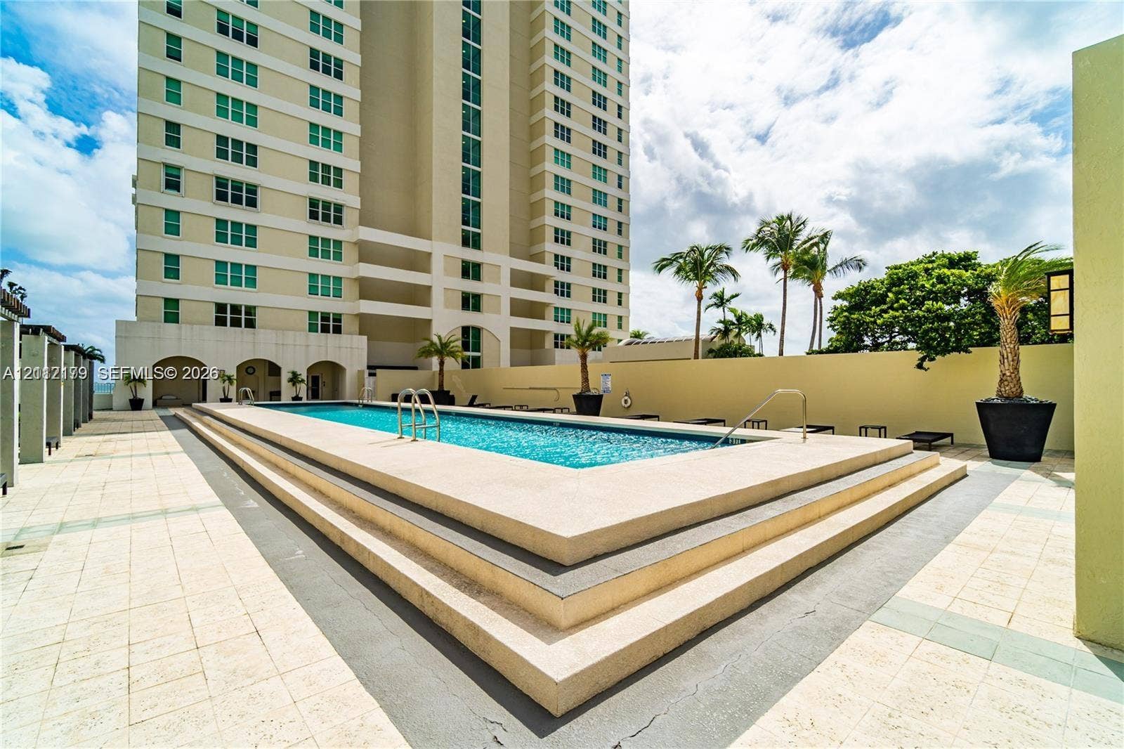800 Claughton Island Drive, #1604, Miami, Miami, FL 33131 Elevated swimming pool featuring a stepped concrete surround, tile-finished pool deck, and palm tree landscaping