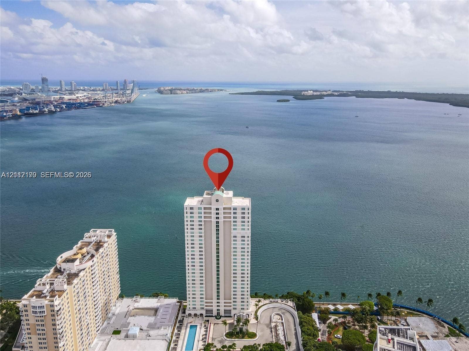 800 Claughton Island Drive, #1604, Miami, Miami, FL 33131 Aerial perspective of a high-rise waterfront building featuring an outdoor swimming pool, paved surface parking, and extensive shoreline exposure