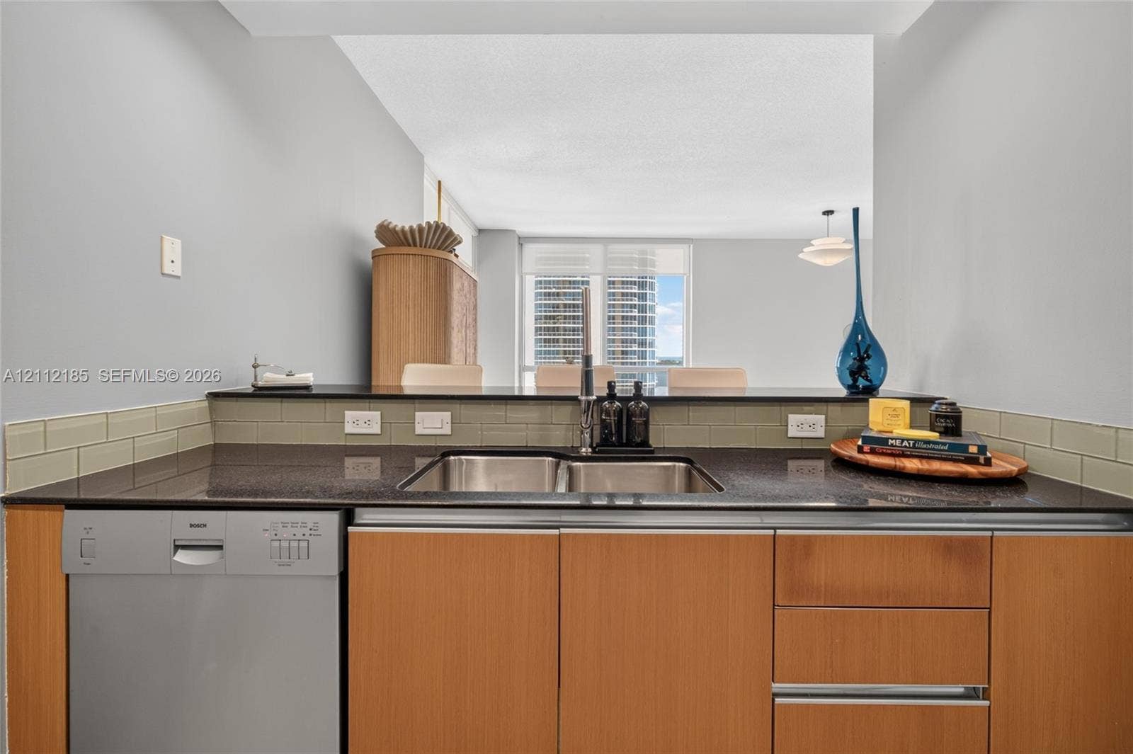 1060 Brickell Avenue, #2401, Miami, FL 33131 Kitchen featuring flat-panel wood-finish cabinetry, dark solid-surface countertops, a stainless steel dual-basin undermount sink, and a subway tile backsplash