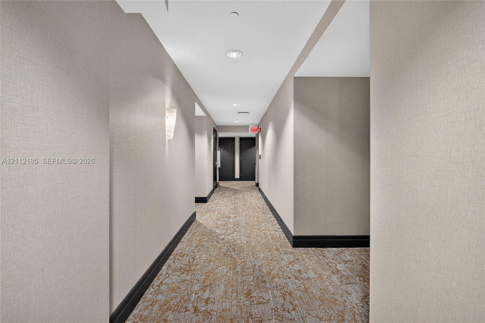 1060 Brickell Avenue, #2401, Miami, FL 33131 Hallway featuring textured neutral wall covering, patterned carpeted flooring, contrasting dark trim, and wall-mounted sconce lighting
