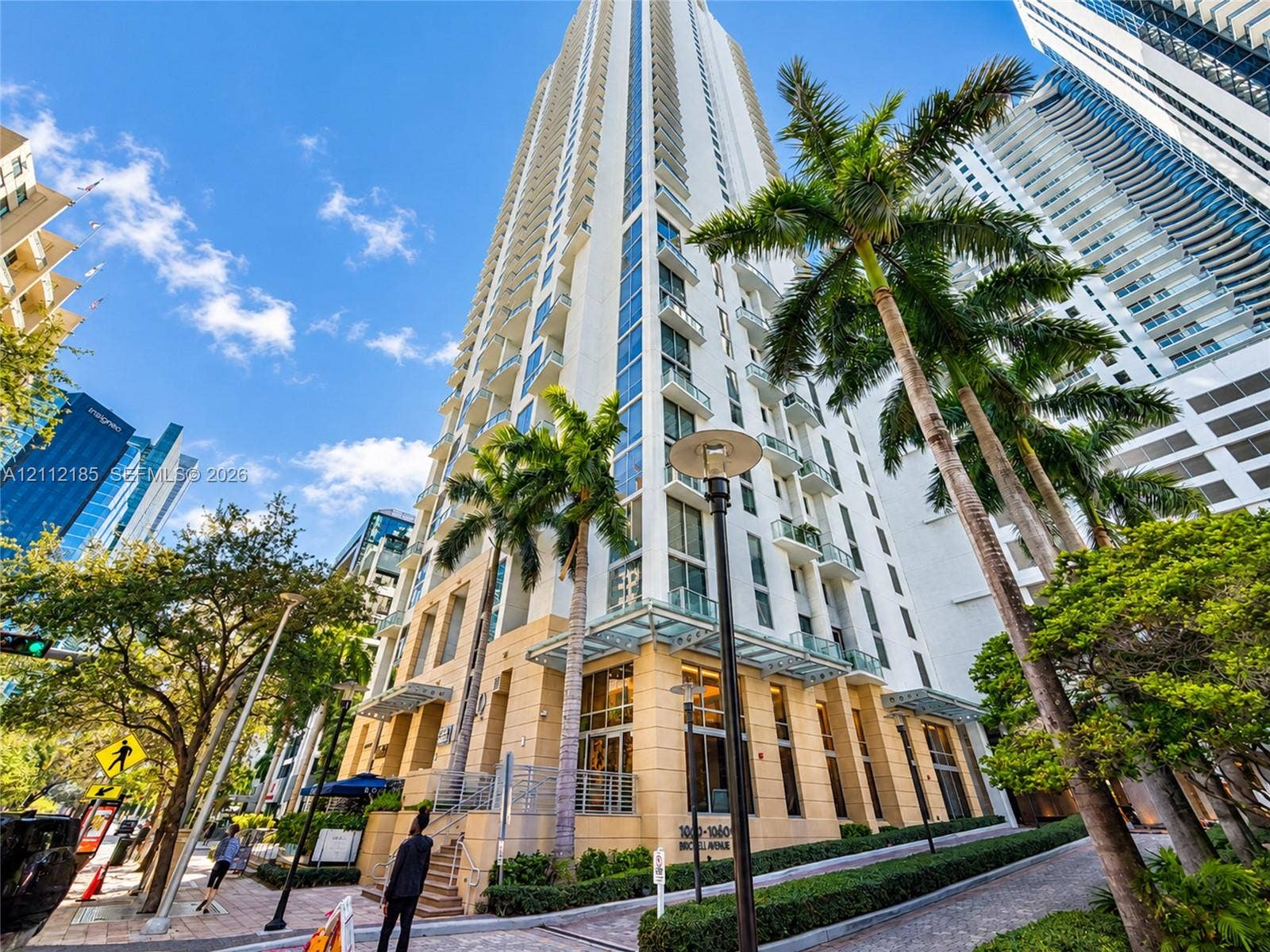 1060 Brickell Avenue, #2401, Miami, FL 33131 High-rise building exterior featuring a light-toned masonry facade, floor-to-ceiling glass paneling, stacked private balconies, and glass-canopy entryway detailing