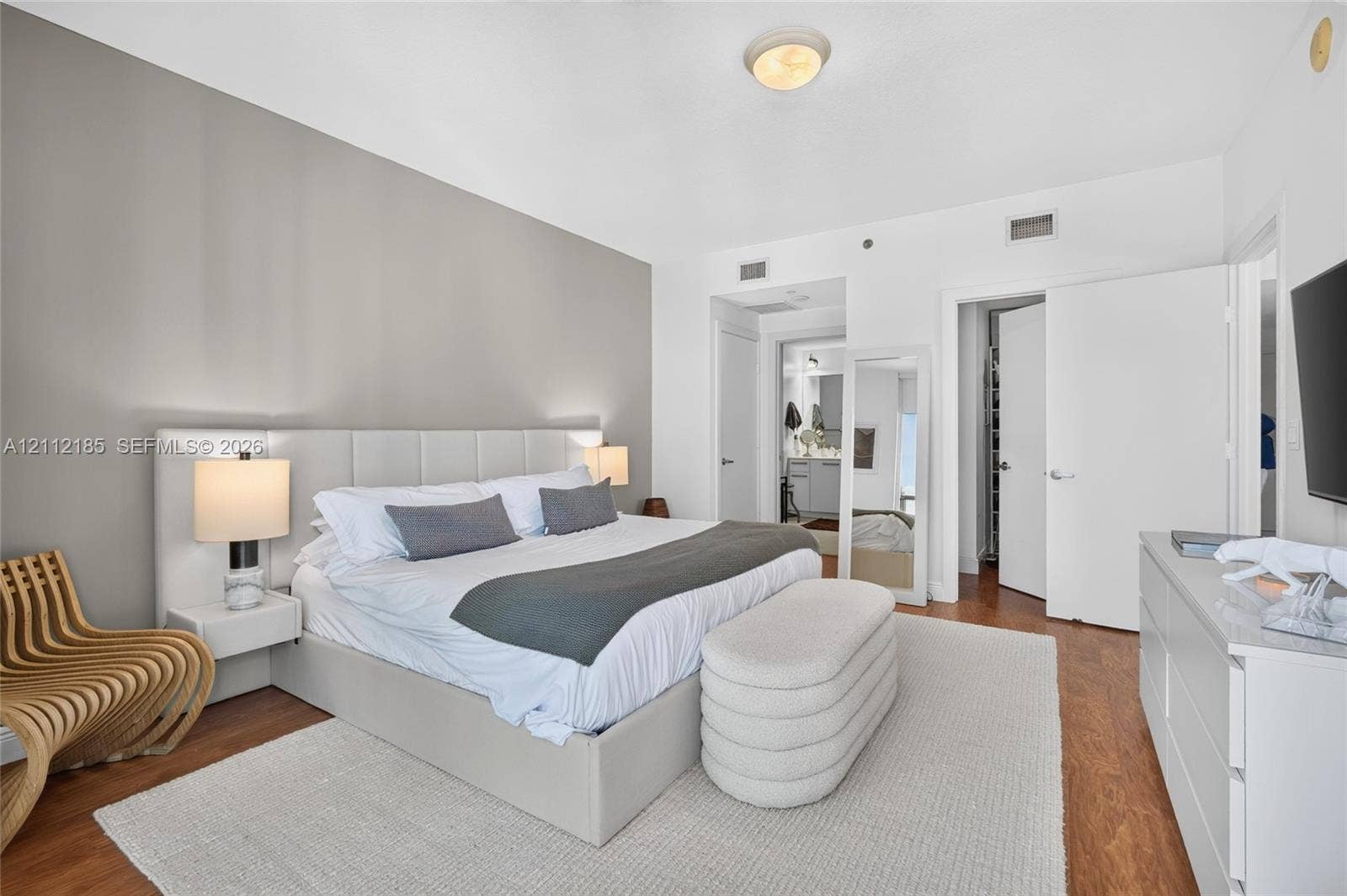 1060 Brickell Avenue, #2401, Miami, FL 33131 Neutral-toned room featuring wood-finish flooring, a contemporary floating headboard with integrated side tables, and multiple interior door access points