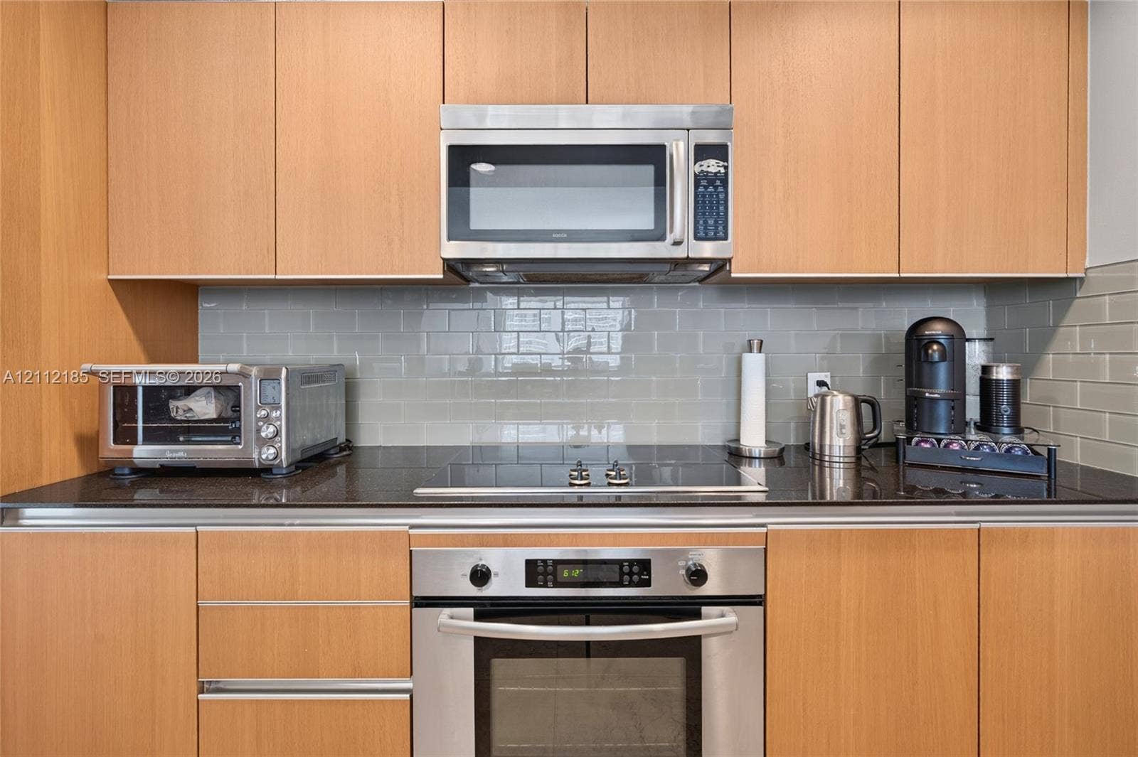 1060 Brickell Avenue, #2401, Miami, FL 33131 Kitchen featuring light wood-finish flat-panel cabinetry, dark stone countertops, stainless steel built-in oven, integrated microwave, and a glass subway tile backsplash