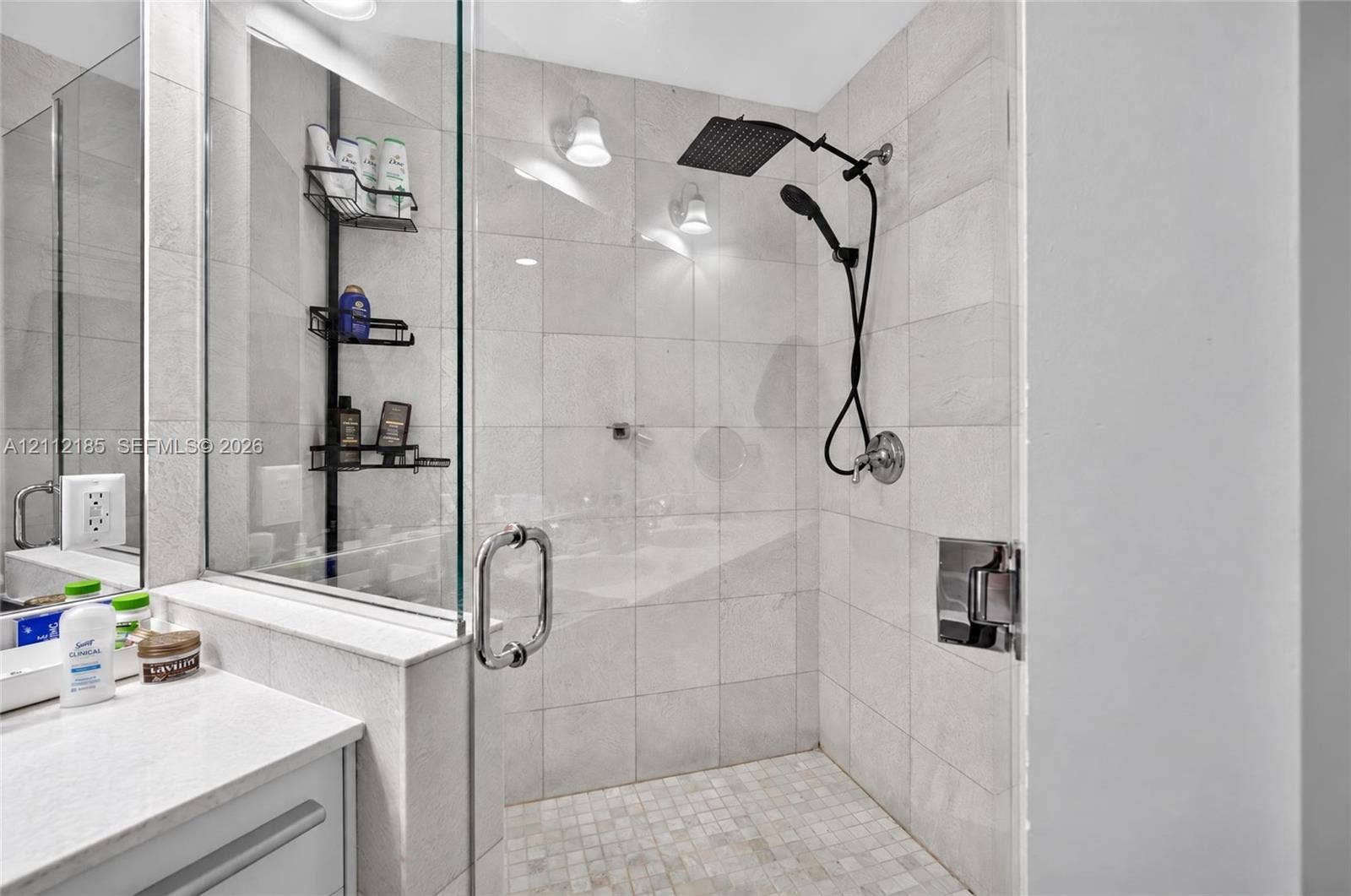 1060 Brickell Avenue, #2401, Miami, FL 33131 Walk-in shower featuring light-toned tile wall surround, mosaic tile floor, glass enclosure, and dual-function matte black showerhead