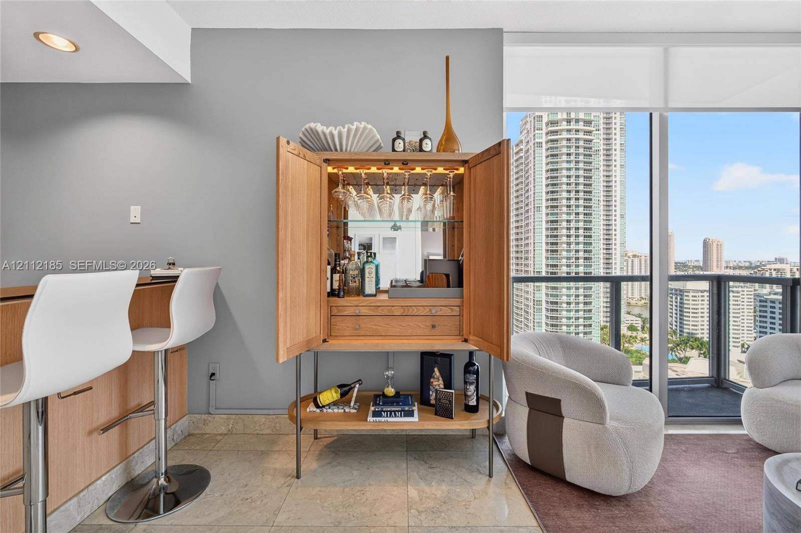 1060 Brickell Avenue, #2401, Miami, FL 33131 Floor-to-ceiling windows with urban exposure, tile flooring, and integrated wood-finished bar cabinetry featuring mirrored backing and overhead glass storage