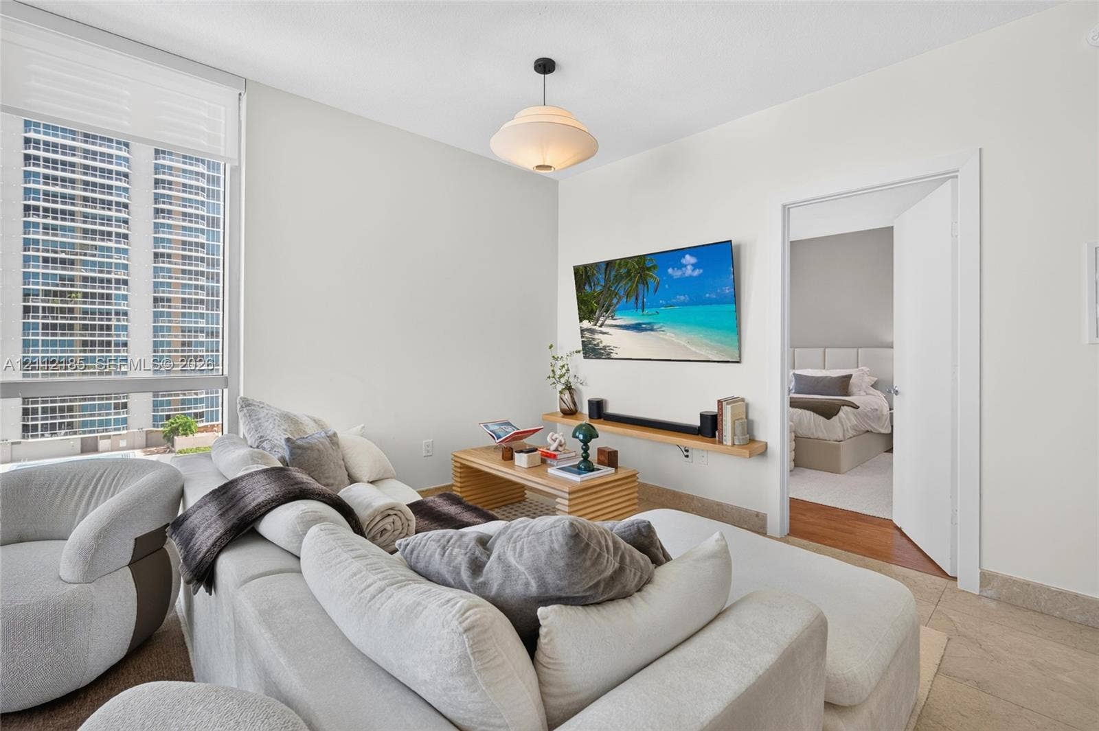 1060 Brickell Avenue, #2401, Miami, FL 33131 Large floor-to-ceiling windows, wall-mounted natural wood floating shelf, semi-flush mount pendant lighting, and neutral stone-finish flooring