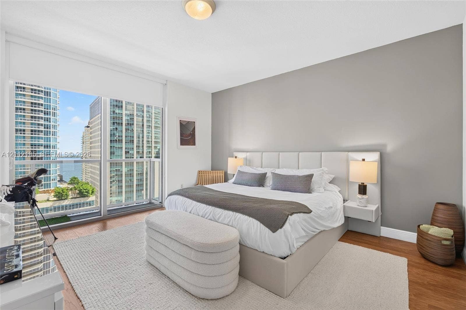 1060 Brickell Avenue, #2401, Miami, FL 33131 Bedroom featuring floor-to-ceiling windows, wood-finish flooring, a neutral accent wall, and a custom built-in headboard with integrated floating nightstands