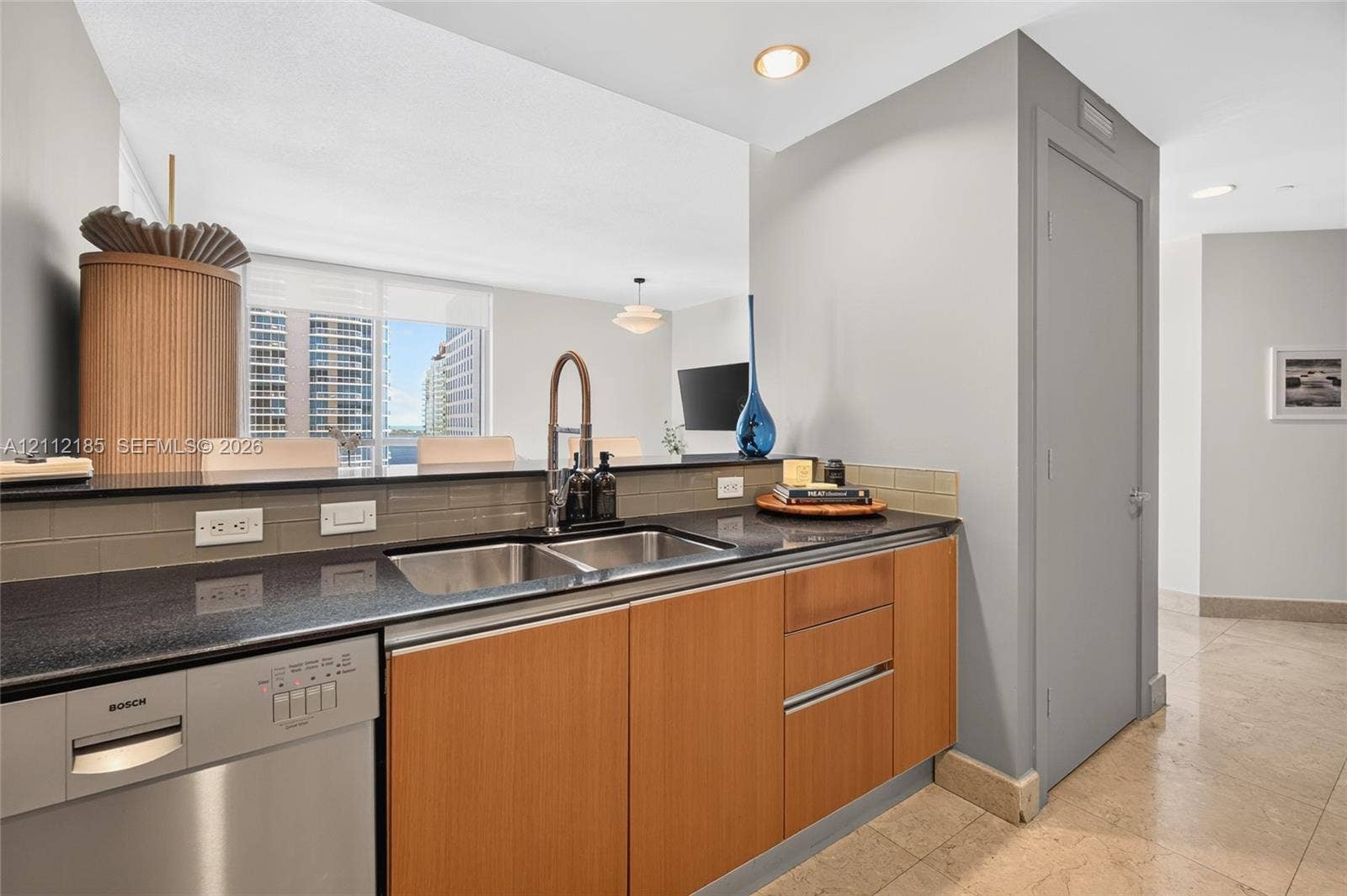 1060 Brickell Avenue, #2401, Miami, FL 33131 Kitchen area featuring stone countertops, natural wood-finish cabinetry, stainless steel dishwasher, undermount dual-basin sink with pull-down faucet, and neutral subway tile backsplash