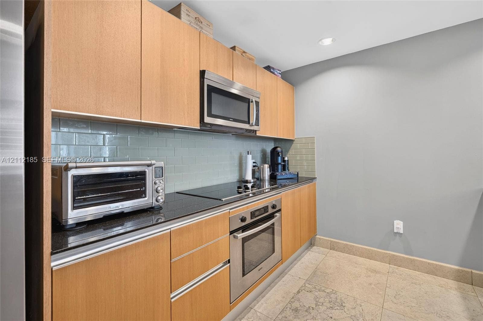 1060 Brickell Avenue, #2401, Miami, FL 33131 Kitchen featuring flat-panel wood cabinetry, black countertops, a subway tile backsplash, stainless steel appliances, and tile flooring