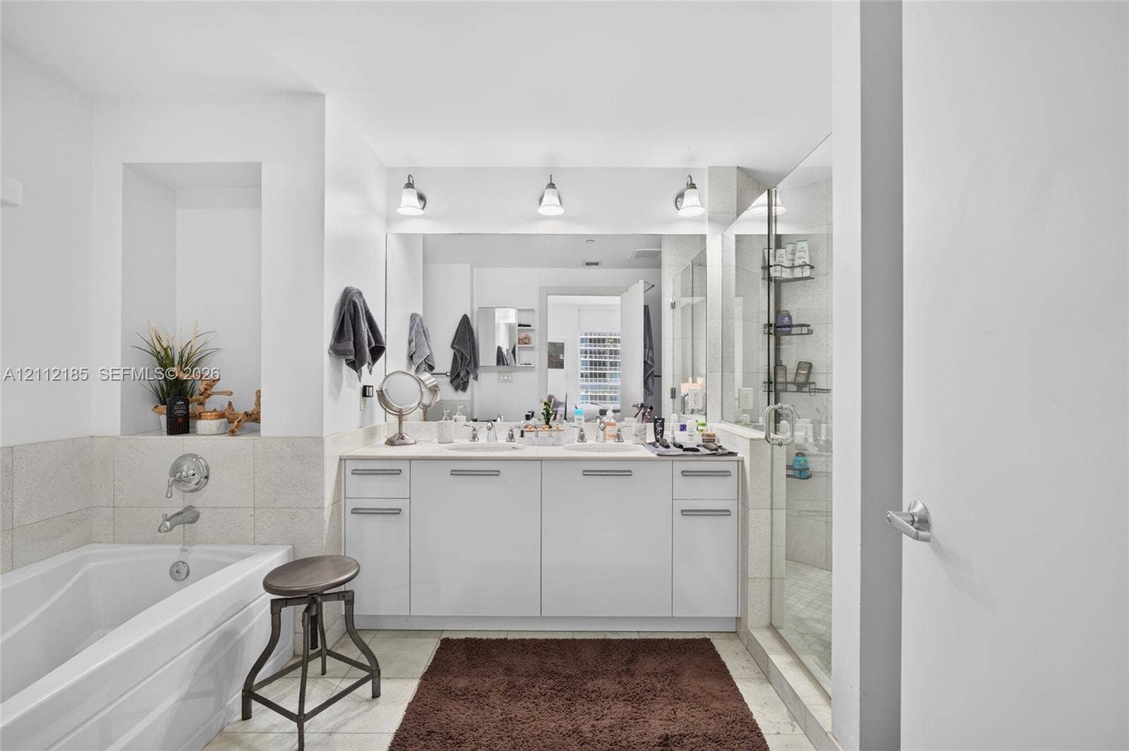 1060 Brickell Avenue, #2401, Miami, FL 33131 Bathroom featuring dual-sink vanity with light-toned cabinetry, built-in recessed wall shelving, soaking tub with wall-mounted chrome fixtures, and glass-enclosed shower with tiled surround