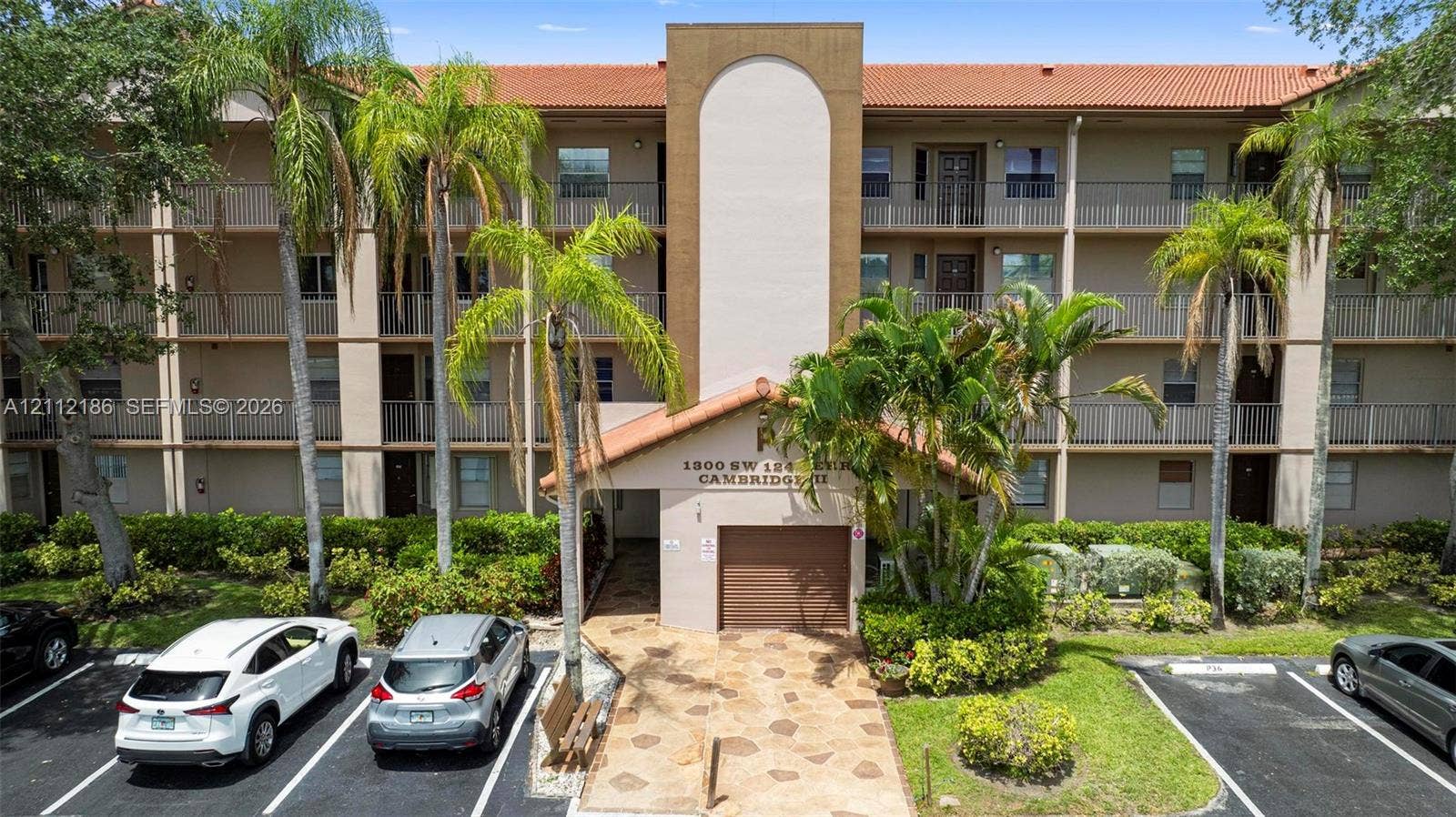 1300 SW 124th Terrace, #107P, Pembroke Pines, Pembroke Pines, FL 33027 Multi-story residential building featuring a terracotta tile roof, stucco exterior, private covered balconies, and stone-paver walkway