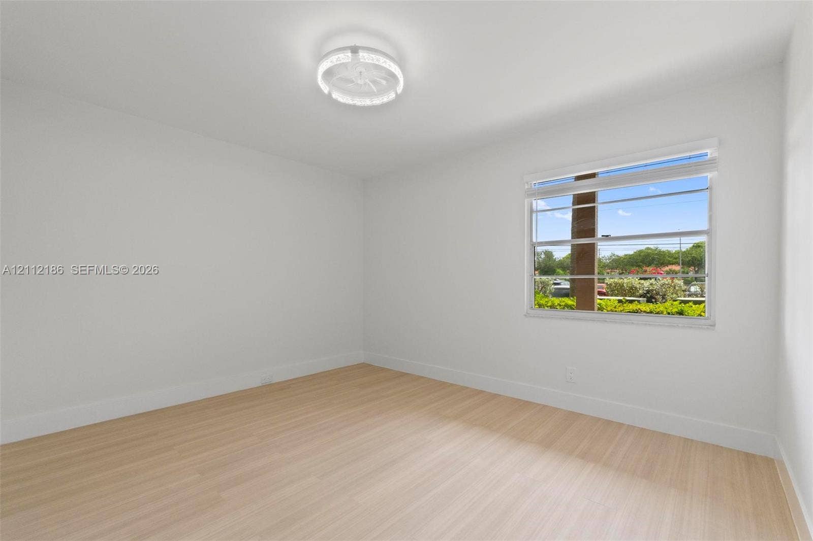 1300 SW 124th Terrace, #107P, Pembroke Pines, Pembroke Pines, FL 33027 Light-filled room featuring wood-finish flooring, crisp neutral walls, and a modern circular LED flush-mount fixture