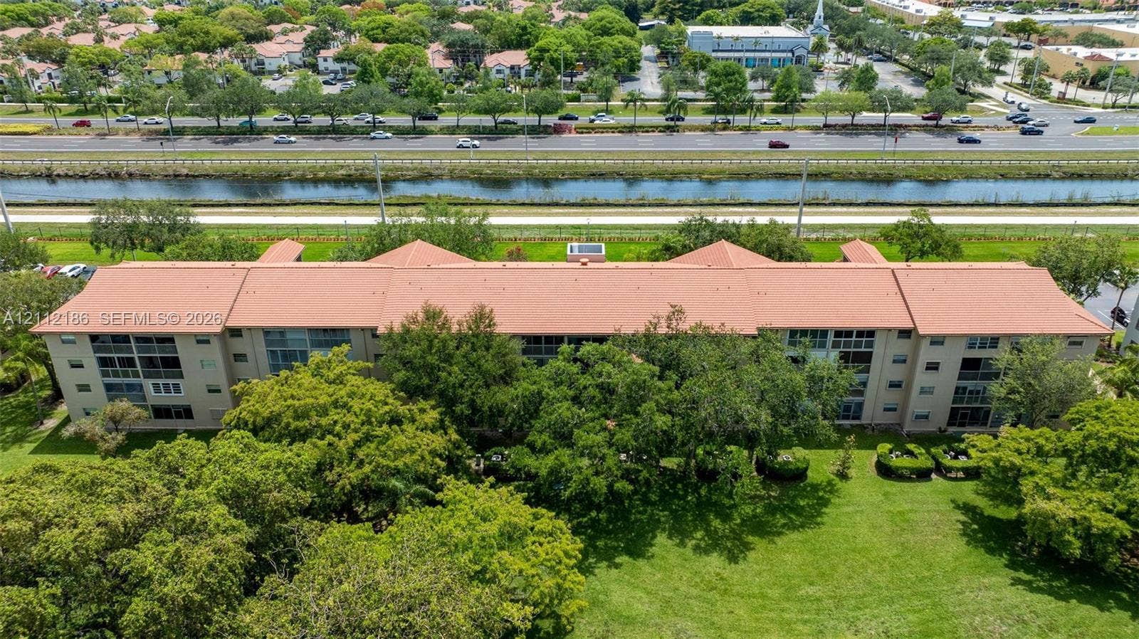 1300 SW 124th Terrace, #107P, Pembroke Pines, Pembroke Pines, FL 33027 Multi-story building featuring a tile roof, screened-in balcony enclosures, and expansive surrounding green space with mature trees