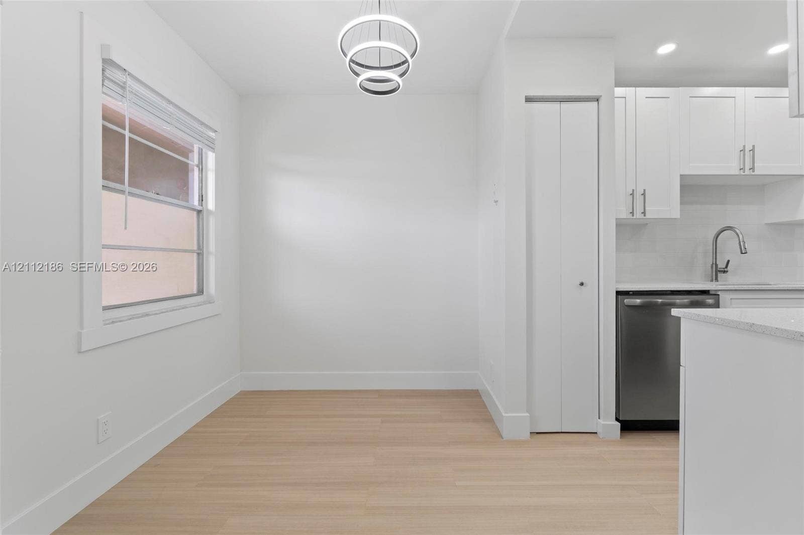 1300 SW 124th Terrace, #107P, Pembroke Pines, Pembroke Pines, FL 33027 Light-filled area featuring wood-finish flooring, a modern three-ring pendant light, a recessed folding-door closet, and white cabinetry with a stainless steel dishwasher