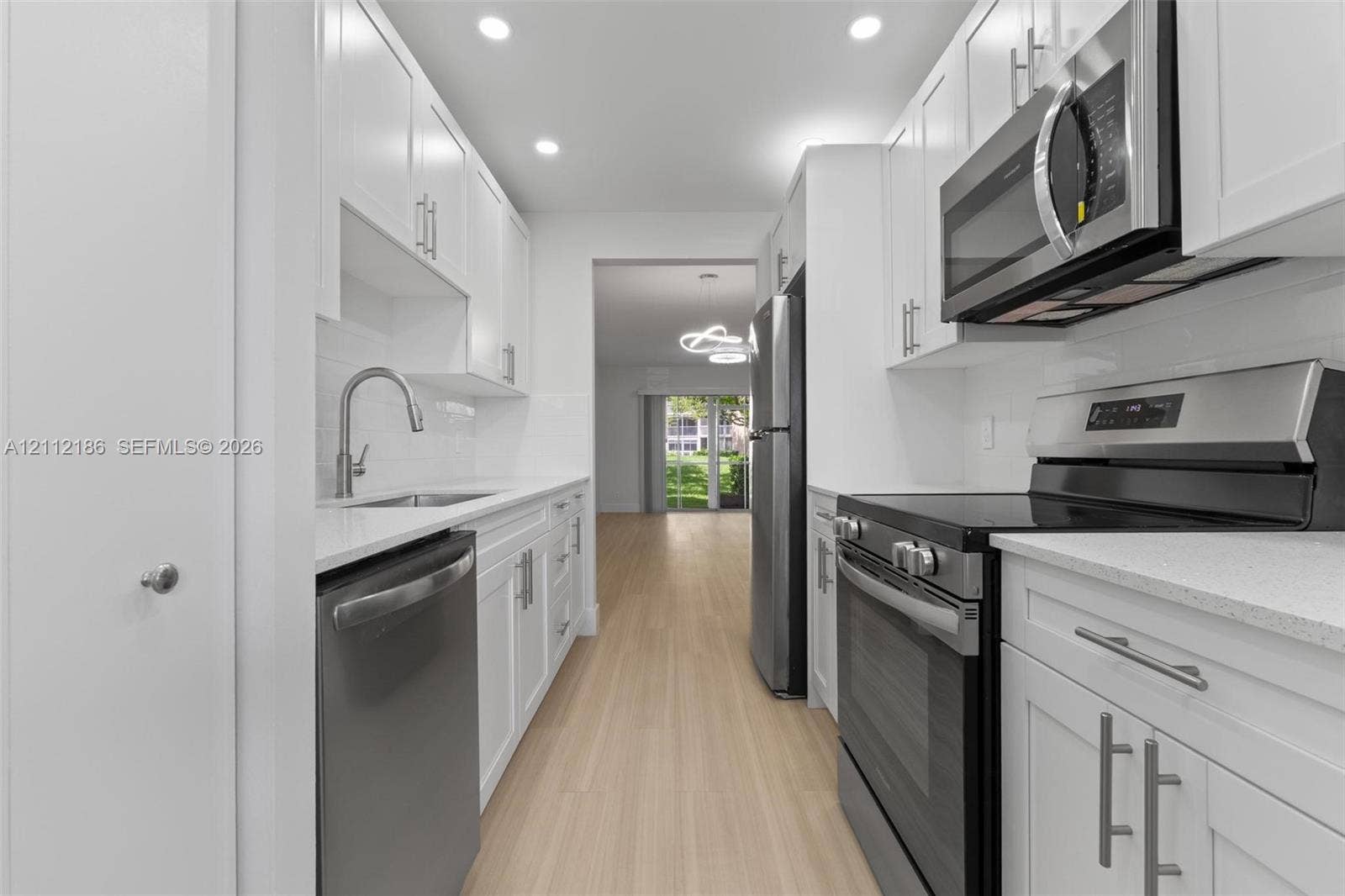 1300 SW 124th Terrace, #107P, Pembroke Pines, Pembroke Pines, FL 33027 Kitchen featuring white shaker-style cabinetry, stainless steel appliances, quartz countertops, tile backsplash, and wood-finish flooring