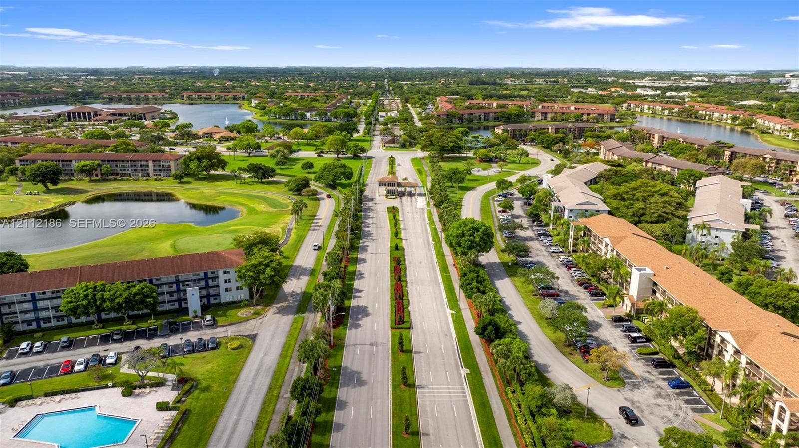 1300 SW 124th Terrace, #107P, Pembroke Pines, Pembroke Pines, FL 33027 Aerial perspective of a multi-building community featuring multiple water features, manicured green space, paved parking areas, and an outdoor swimming pool