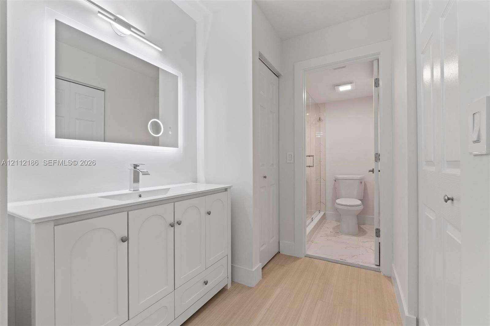 1300 SW 124th Terrace, #107P, Pembroke Pines, Pembroke Pines, FL 33027 White vanity with integrated sink, backlit LED mirror, wood-finish flooring, and walk-in shower with glass enclosure