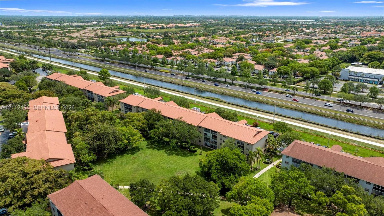 1300 SW 124th Terrace, #107P, Pembroke Pines, Pembroke Pines, FL 33027 Aerial perspective of multi-story buildings with terracotta-style roof tiles, featuring landscaped grounds, mature trees, and pedestrian pathways