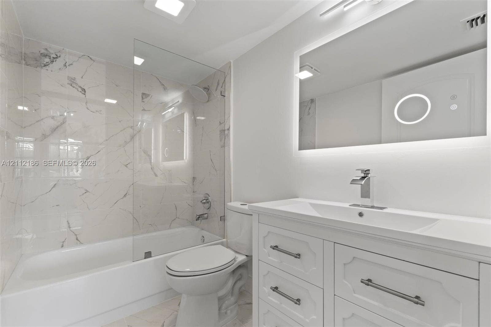 1300 SW 124th Terrace, #107P, Pembroke Pines, Pembroke Pines, FL 33027 Bathroom featuring white custom cabinetry with brushed hardware, stone-finish wall tile surround, glass panel shower enclosure, and integrated LED-backlit mirror