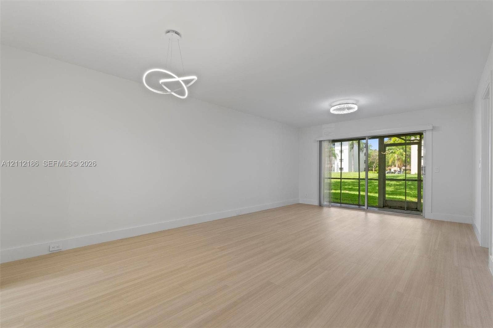 1300 SW 124th Terrace, #107P, Pembroke Pines, Pembroke Pines, FL 33027 Open-concept interior featuring light wood-finish flooring, modern geometric LED pendant lighting, and a sliding glass door providing external access