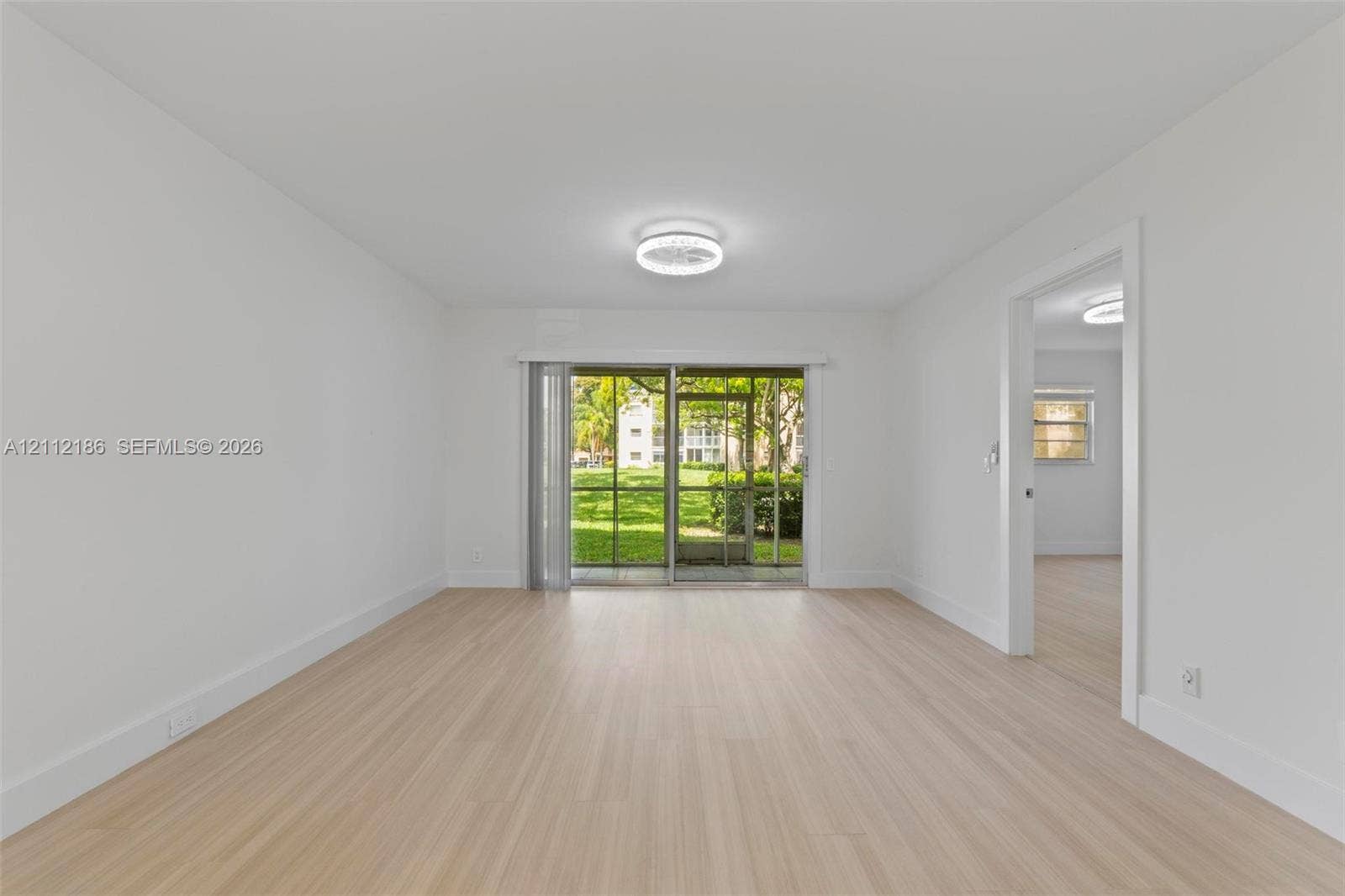 1300 SW 124th Terrace, #107P, Pembroke Pines, Pembroke Pines, FL 33027 Open-concept room featuring light-toned wood-finish flooring, a contemporary flush-mount ceiling fixture, and a sliding glass door providing access to a screened outdoor area