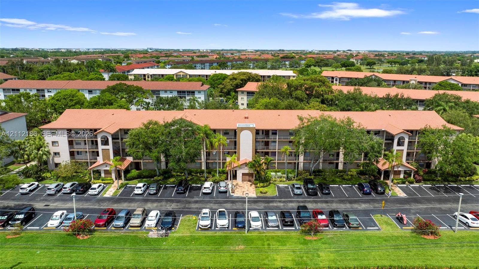 1300 SW 124th Terrace, #107P, Pembroke Pines, Pembroke Pines, FL 33027 Multi-story residential building featuring a terracotta-tiled roof, covered breezeways, exterior balconies, and paved surface parking