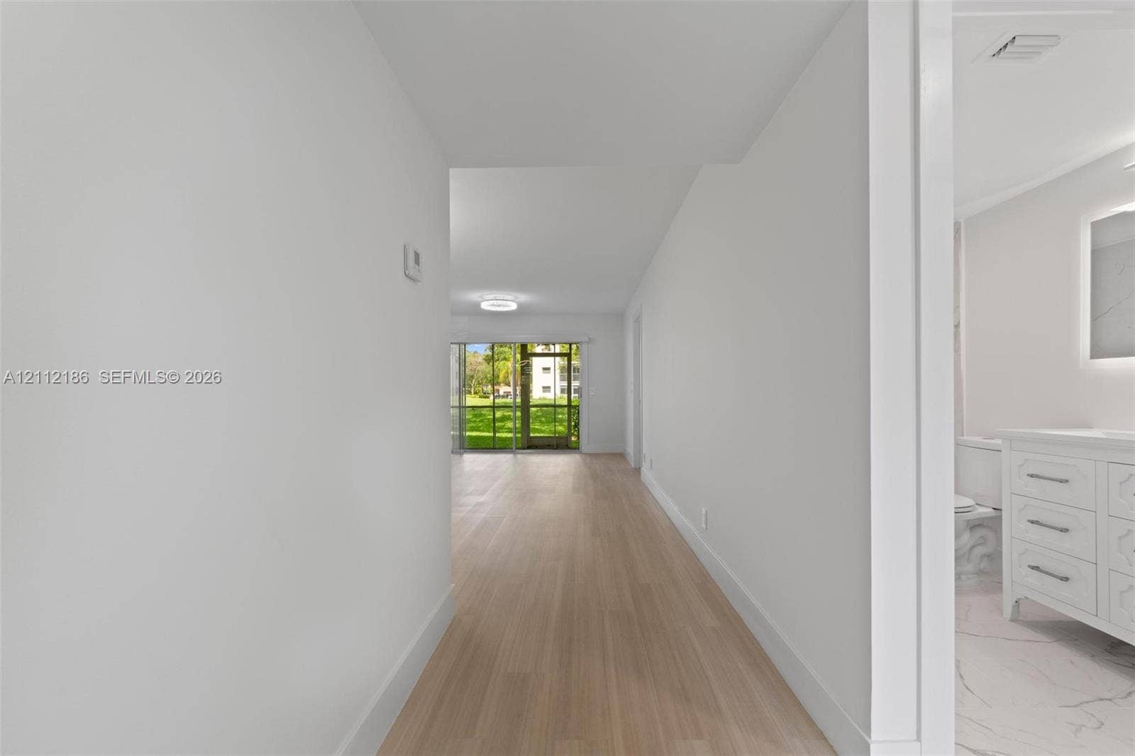 1300 SW 124th Terrace, #107P, Pembroke Pines, Pembroke Pines, FL 33027 Interior hallway featuring light-toned wood-finish flooring and a bathroom vanity with a lighted mirror