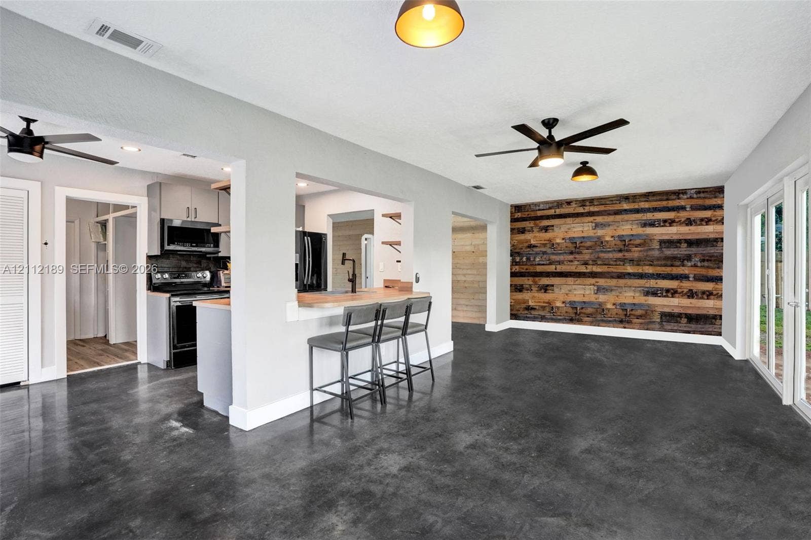 5161 SW 7th Court, #0, Margate, Margate, FL 33068 Open concept living area featuring dark polished concrete flooring, a horizontal reclaimed wood-plank accent wall, ceiling fans, and glass sliding doors