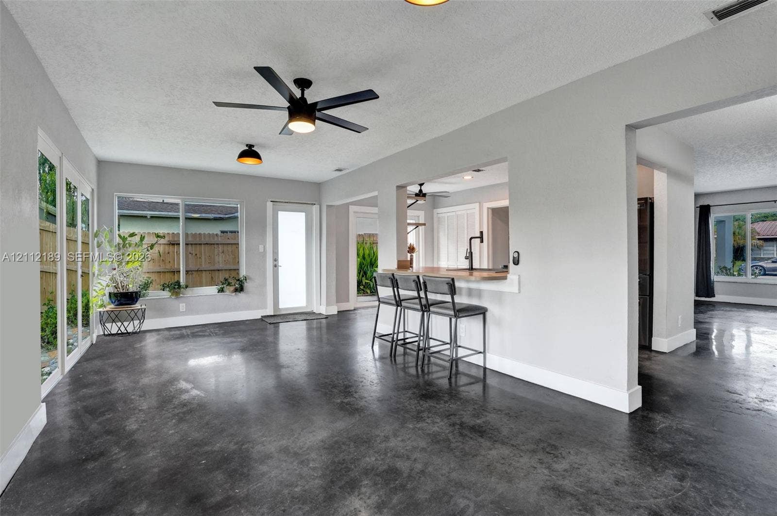 5161 SW 7th Court, #0, Margate, Margate, FL 33068 Polished concrete flooring, pass-through kitchen window with bar seating, matte black ceiling fan, and large windows with natural light exposure