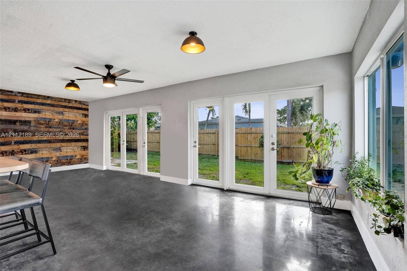 5161 SW 7th Court, #0, Margate, Margate, FL 33068 Polished concrete flooring, accent wall with horizontal wood planks, multiple sets of white-framed glass doors, and modern industrial-style ceiling fixtures