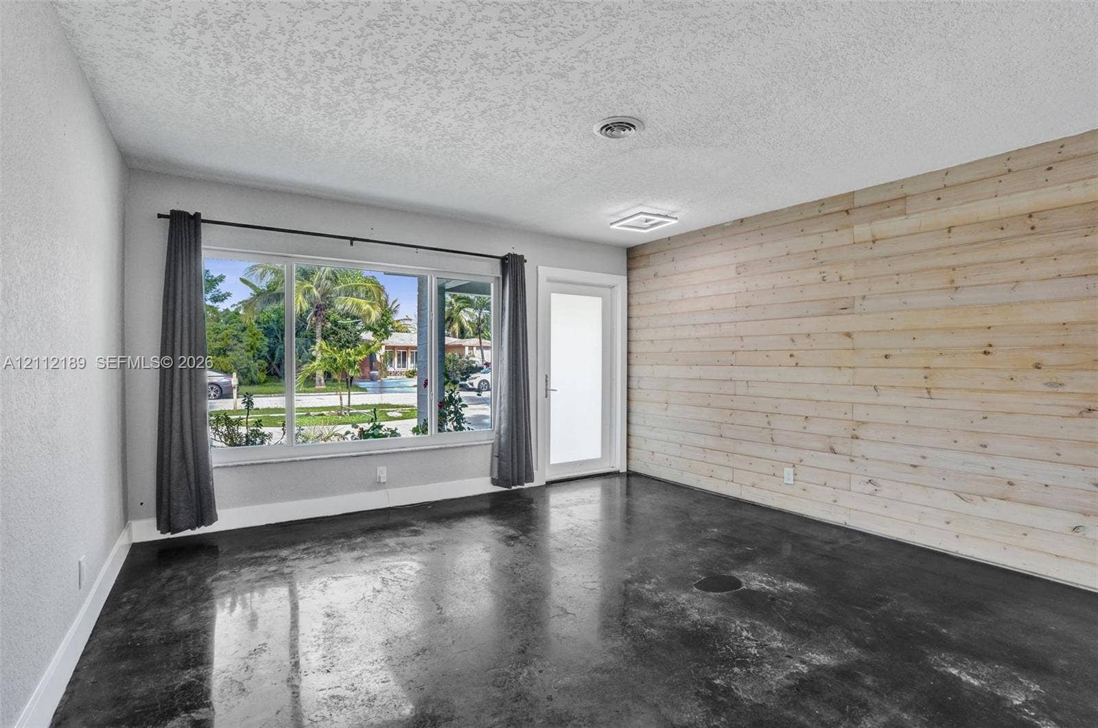 5161 SW 7th Court, #0, Margate, Margate, FL 33068 Interior space featuring a horizontal wood-plank accent wall, polished concrete flooring, large multi-pane window, and glass-paneled exterior door
