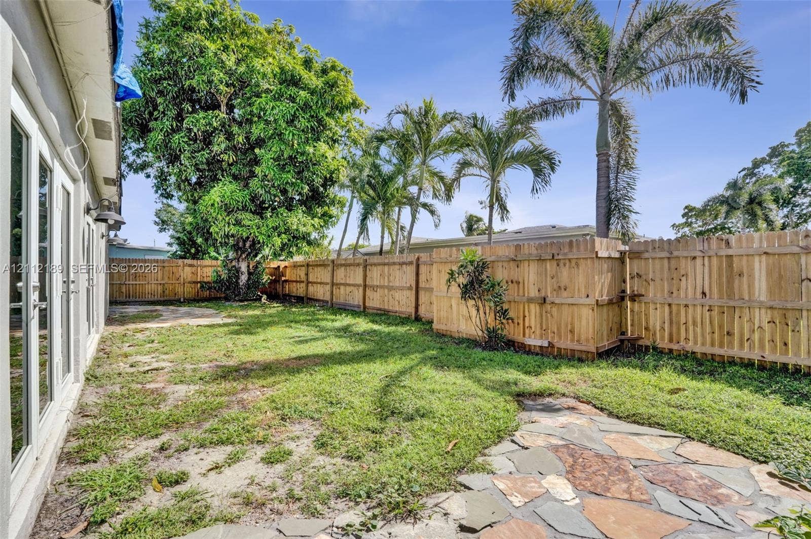 5161 SW 7th Court, #0, Margate, Margate, FL 33068 Backyard featuring a wood privacy fence, flagstone patio, lawn area, and mature palm trees