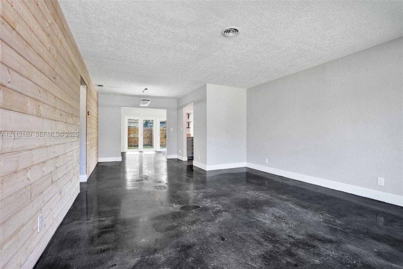 5161 SW 7th Court, #0, Margate, Margate, FL 33068 Interior space featuring polished concrete flooring, horizontal wood-plank accent wall, and double glass-paned exterior doors