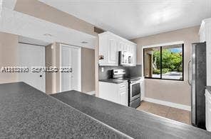 440 Lakeview Drive, #103, Weston, Weston, FL 33326 Kitchen featuring a dark-toned laminate countertop peninsula, white shaker-style cabinetry, stainless steel appliances, and tile flooring