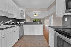 440 Lakeview Drive, #103, Weston, Weston, FL 33326 Kitchen featuring white shaker-style cabinetry, dark stone-finish countertops, stainless steel appliances, ceramic tile flooring, and a glass-front display cabinet