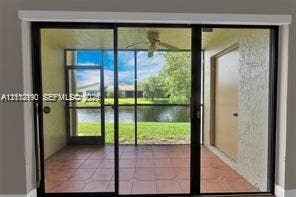 440 Lakeview Drive, #103, Weston, Weston, FL 33326 Screened-in lanai featuring tiled flooring, a ceiling fan, and sliding glass door access, opening to a waterfront backdrop