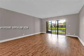 440 Lakeview Drive, #103, Weston, Weston, FL 33326 Spacious living area featuring wood-finish flooring, neutral wall paint, and floor-to-ceiling glass sliding doors opening to a screened enclosure