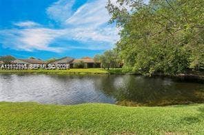 440 Lakeview Drive, #103, Weston, Weston, FL 33326 Waterfront property featuring a manicured lawn, mature trees, and shingled roofing