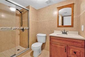 440 Lakeview Drive, #103, Weston, Weston, FL 33326 Bathroom featuring a wood-tone vanity cabinet, stone-surfaced countertop, integrated sink, walk-in glass-enclosed shower, and wall-mounted wooden mirror frame