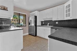 440 Lakeview Drive, #103, Weston, Weston, FL 33326 Kitchen featuring white cabinetry with glass-panel display doors, built-in wine storage, stainless steel refrigerator, dark solid-surface countertops, and tiled flooring