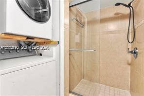 440 Lakeview Drive, #103, Weston, Weston, FL 33326 Shower stall featuring a frameless glass door, wall-mounted handheld showerhead, and tiled walls, accompanied by built-in laundry appliances with wood-finish shelving