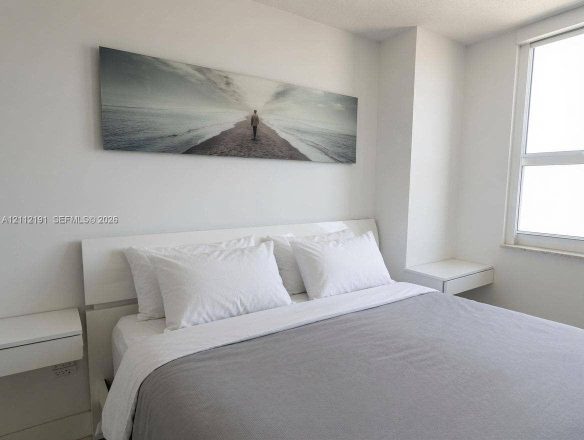 Neutral-toned interior featuring smooth wall finishes, a large multi-pane window, and dual wall-mounted floating bedside surfaces