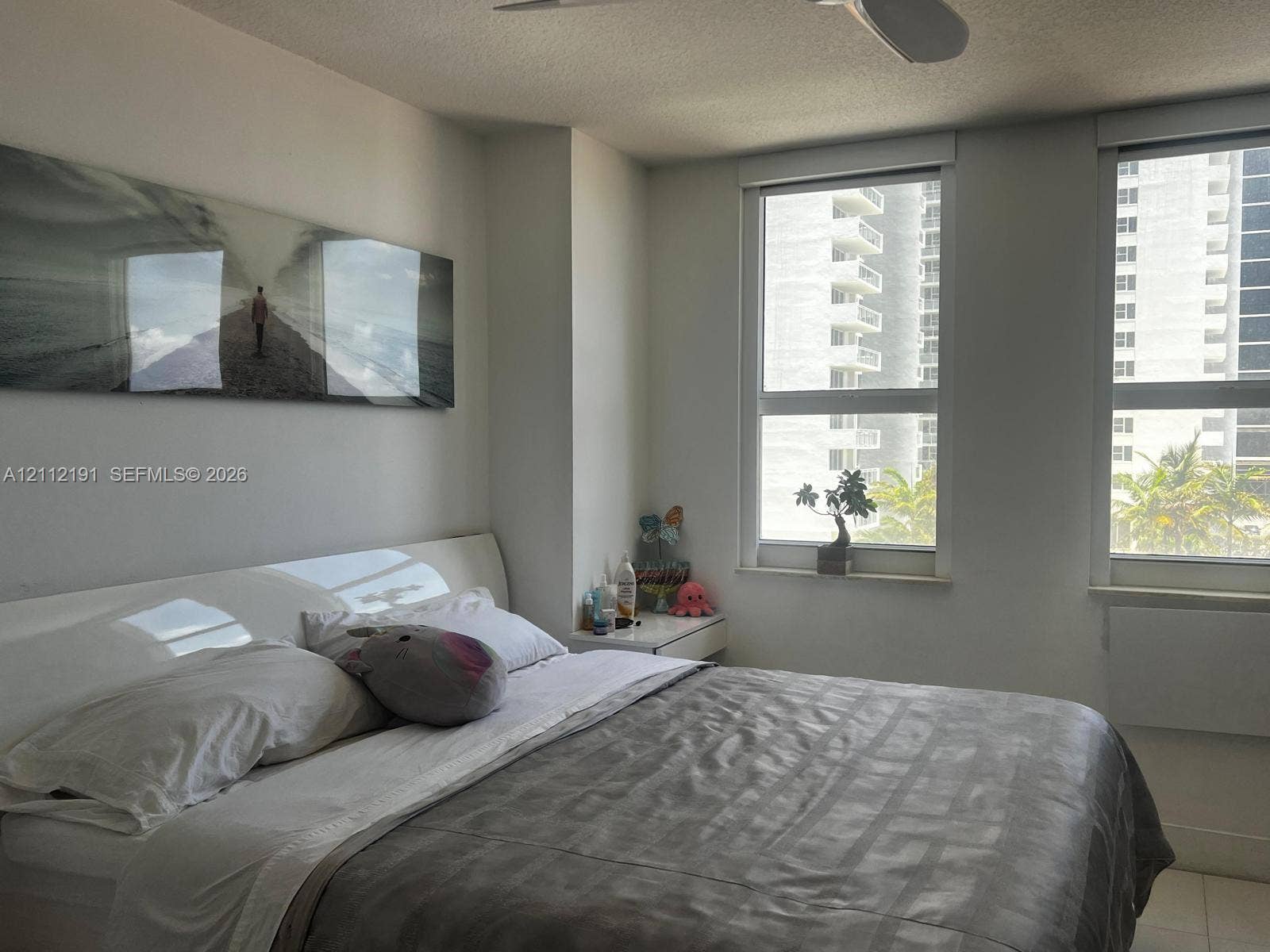 Neutral-toned interior featuring dual oversized windows, light-colored tile flooring, and a white ceiling-mounted fan