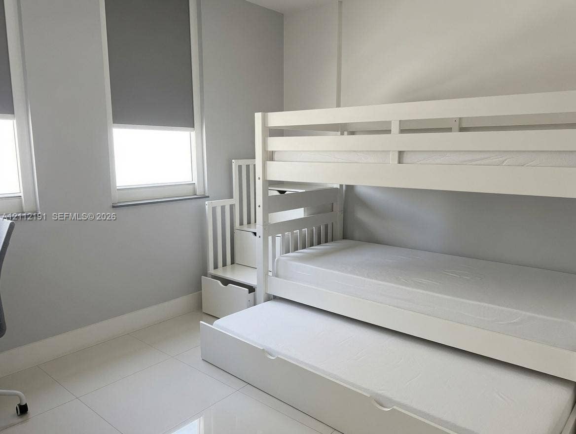 Neutral-toned room featuring large windows with roller shades, smooth-finish ceramic tile flooring, and light-reflecting wall paint