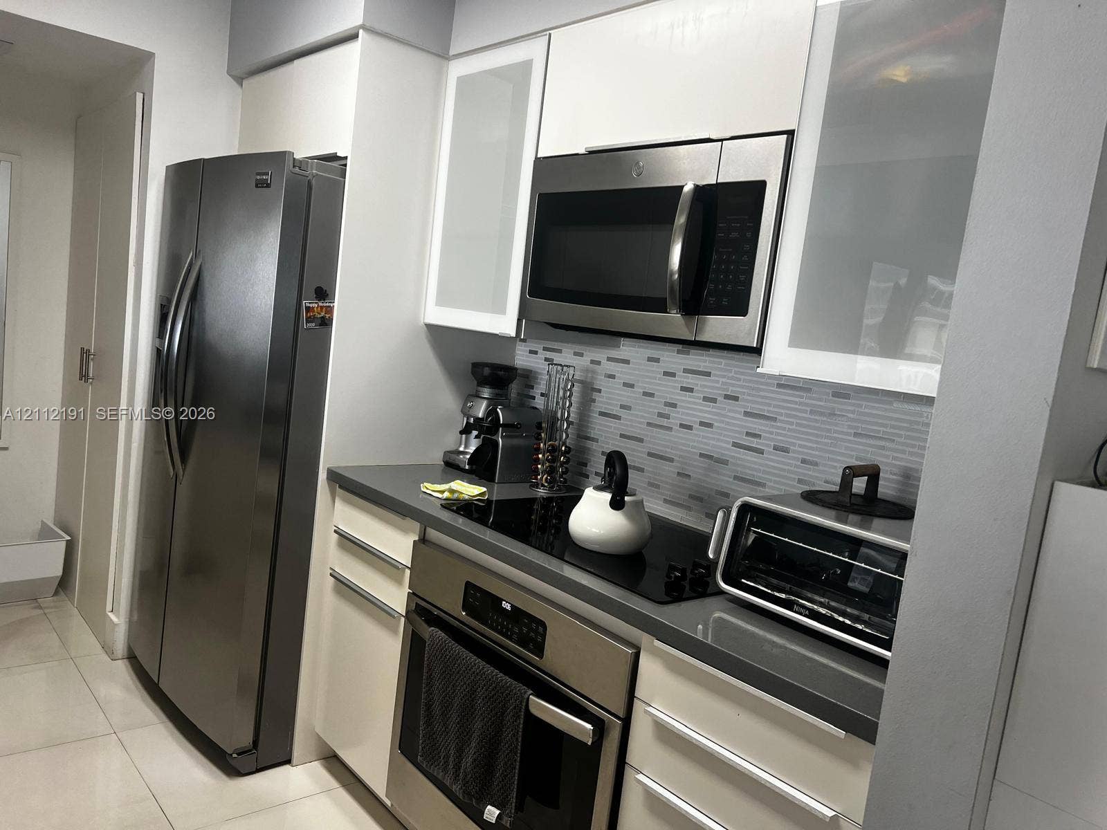 Kitchen featuring white cabinetry with frosted glass inserts, stainless steel appliances, a stone-composite countertop, and a glass-tile backsplash