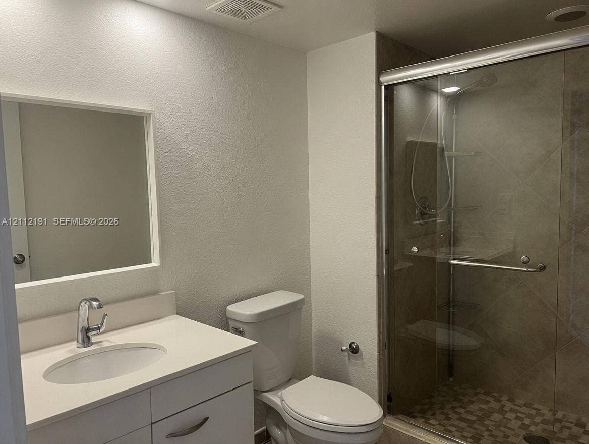 Bathroom featuring a white vanity cabinet, solid-surface countertop with an integrated basin, framed wall mirror, and a walk-in shower with a sliding glass door and tile surround