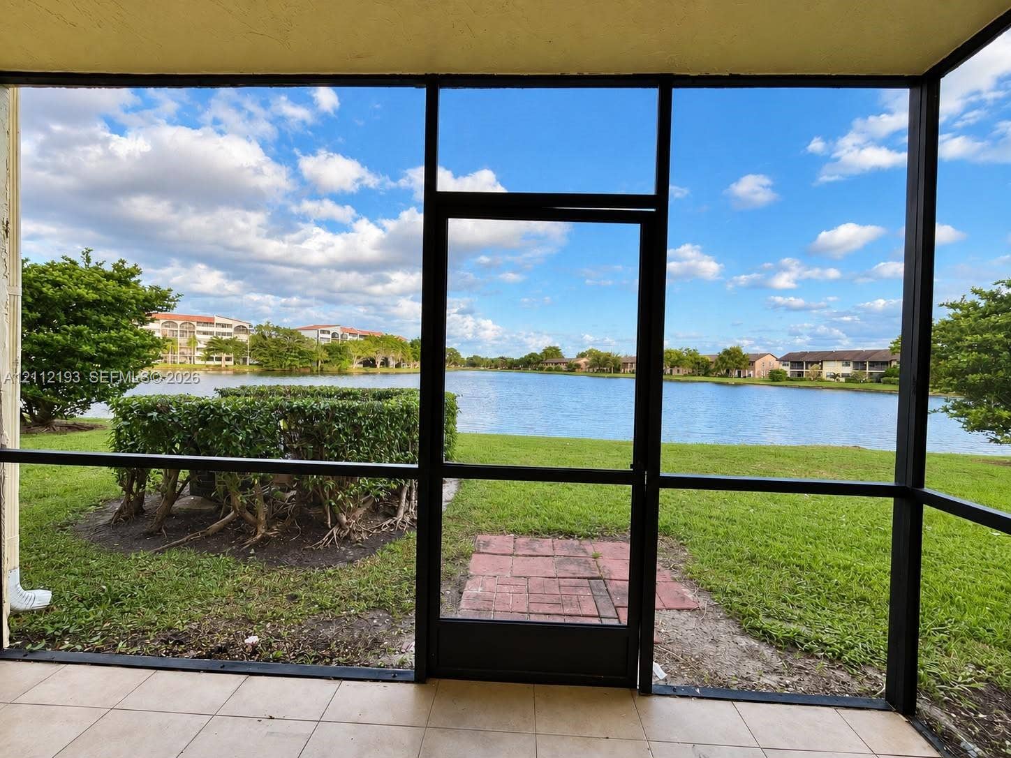10013 Winding Lake Road, #106, Sunrise, Sunrise, FL 33351 Screened-in patio with tile flooring, featuring metal framing, a direct exit to a grass yard, and a brick paver landing