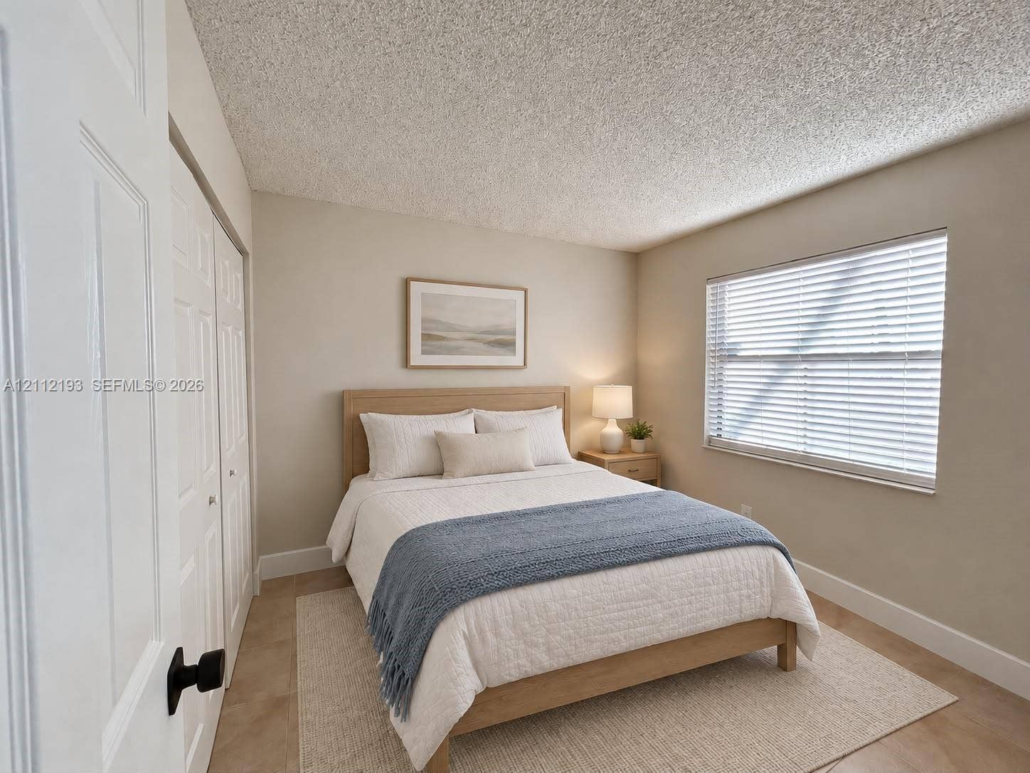 10013 Winding Lake Road, #106, Sunrise, Sunrise, FL 33351 Neutral interior featuring light-toned flooring, textured ceiling, dual-panel closet doors with matte black hardware, and a window equipped with horizontal blinds