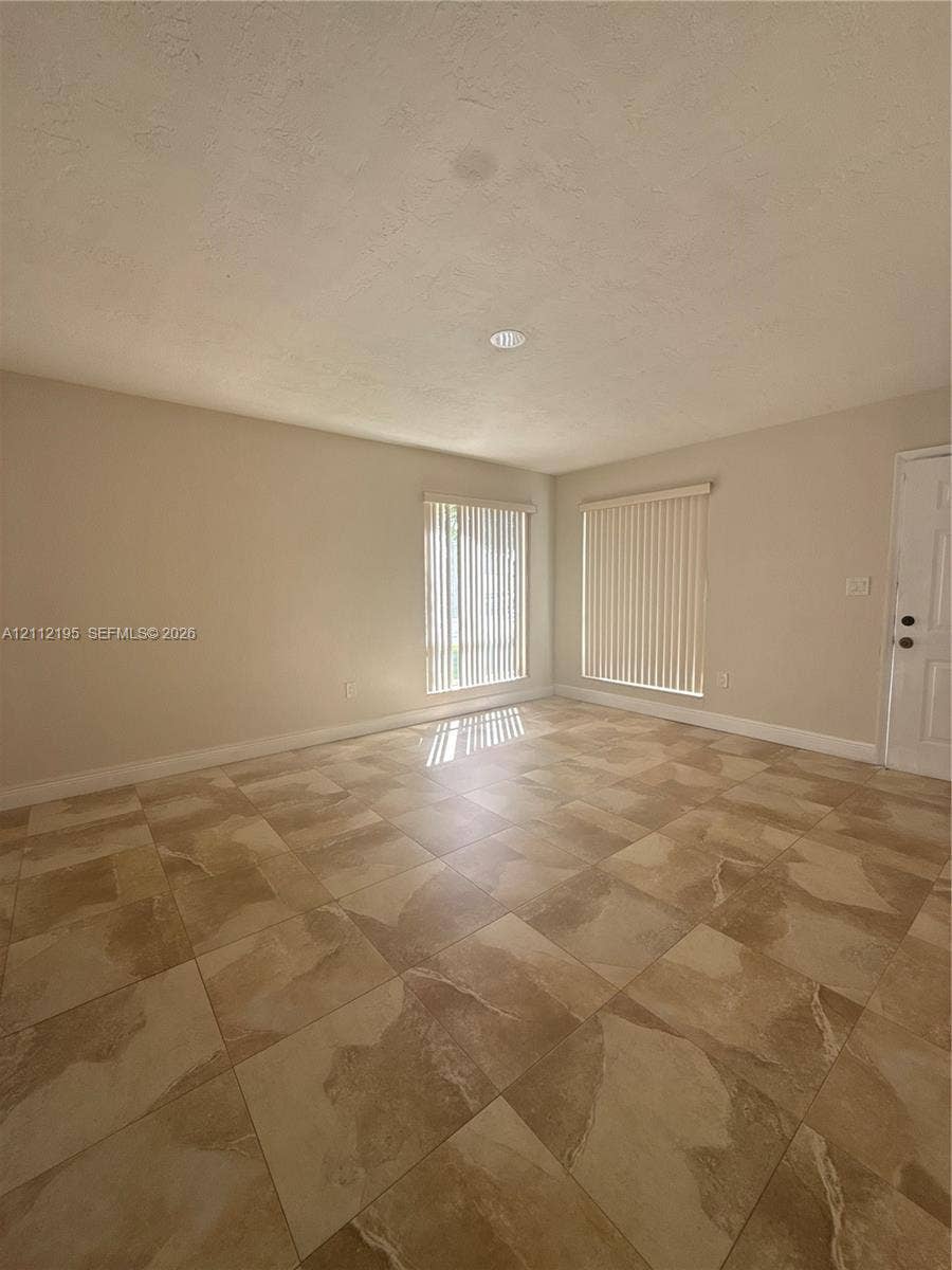 11745 SW 122nd Place, #11745, Miami, Miami, FL 33186 Neutral-toned interior space featuring large-format ceramic tile flooring, two windows with vertical blinds, and a recessed ceiling light fixture