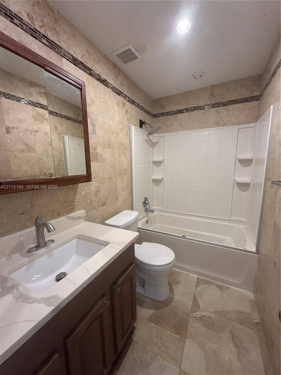 11745 SW 122nd Place, #11745, Miami, Miami, FL 33186 Bathroom featuring stone-finish wall and floor tiling, a vanity with a white countertop and rectangular undermount sink, a framed medicine cabinet, and a bathtub with a white surround
